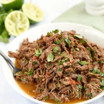 Instant Pot Mexican Shredded Beef in a white bowl with limes and a pale green napkin in the background