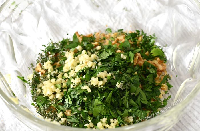 Fresh herbs, garlic and nuts in a large glass bowl.