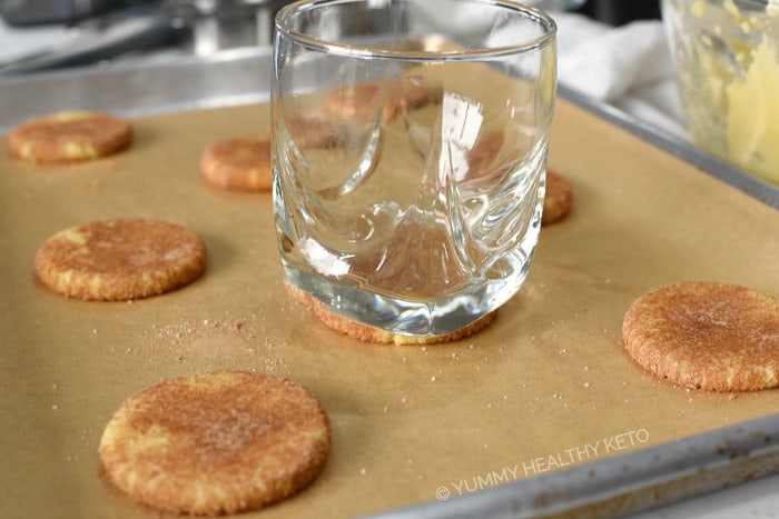 Keto Snickerdoodle Cookies flattened with a glass on a parchment lined baking sheet.