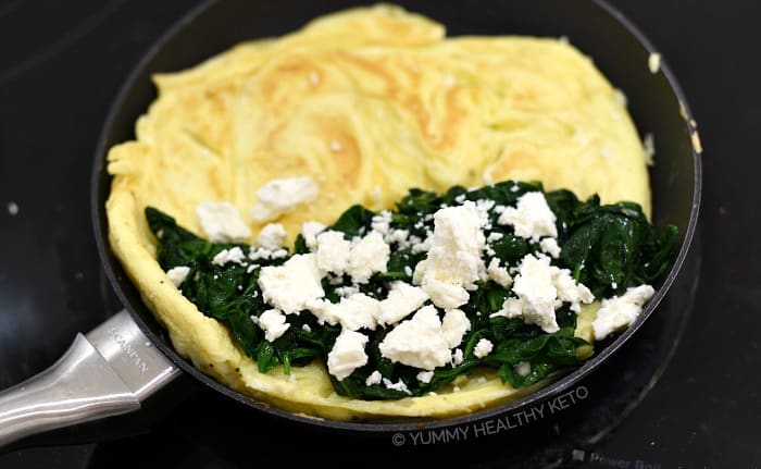 The cooked spinach and crumbled feta on one side of the egg circle.